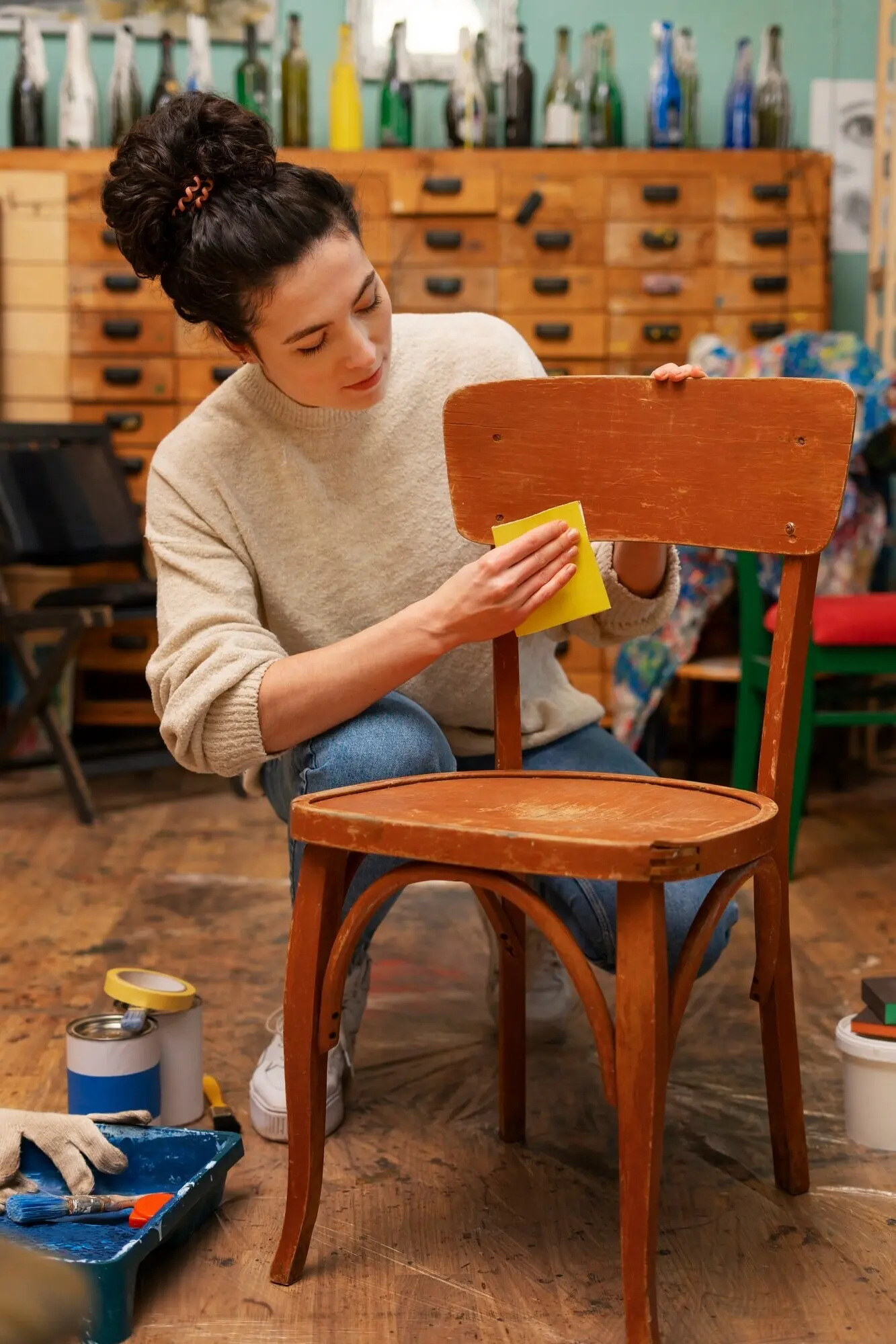 Blick von vorne auf eine Frau, die einen Holzstuhl restauriert.